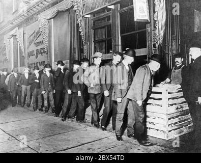 During the night, the Fleischmann bakery distributes free bread leftovers and donations to unemployed and needy people. On Broadway there is a long line of men who came to get bread. Two men supervise the distribution (far right). Stock Photo