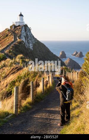 Beautiful asian tourist take some picture at Nugget Point, Dunedin, New Zealand. Young asian traveller enjoys walking in morning along coastline of Ne Stock Photo