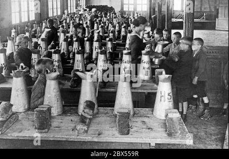 Some poorly clothed children get food and drink in a barren room. On long wooden tables there are jugs of coffee and cocoa, and in front of them are stacks of sliced bread. At the peak of inflation, 3000 city children from poor quarters are accommodated in this Southern German recreation camp, because their parents can no longer feed them. Around 1923. Stock Photo