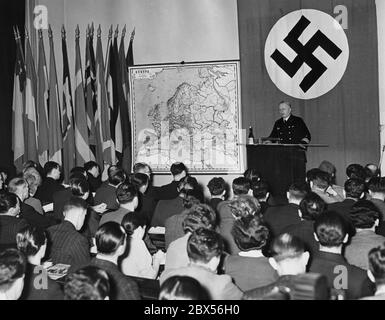The Institute for International Studies at the University of Berlin organized a holiday course named 'Germany at War', in which more than 200 foreign students from 36 different nations are participating. Here a view into the lecture hall during a lecture by Rear Admiral Gladow. On the wall to the left of a swastika flag is a map of Europe and several national flags. Stock Photo