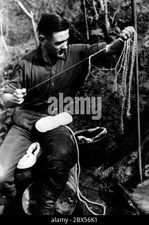 A German soldier makes shoes from the cords of a parachute. During the battle of Kholm, the 'Kampfgruppe Scherer' successfully defended the town for 105 days. (A photo of the Propaganda Company (PK) by war correspondent Richard Muck, who flew into the pocket at the beginning of March). Stock Photo