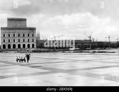 View of the construction site of the Congress Hall designed by the architects Ludwig Ruff and Franz Ruff on the Nuremberg Party Rally Grounds. On the left, a provisional part of the future exterior facade in natural size. On the Grosse Strasse a man pulls a cart. Stock Photo