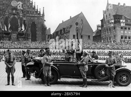 Adolf Hitler talks to Hermann Goering while standing in his Mercedes during the march of the Nazi organizations on the so-called Adolf-Hitler-Platz. On the right Franz Pfeffer von Salomon, on the left Rudolf Hess and Viktor Lutze. In the background the grandstands and the front of Unsere Lieber Frau (Church of Our Lady). Stock Photo