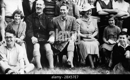 Princess Elizabeth, Captain J.G. Patterson, the camp commander, King George VI, Queen Elizabeth and Princess Margaret Rose watch the boys perform 'Under the Spreading Chestnut Tree' at the Boys Camp. The King is wearing a traditional grey Balmoral Kilt. Stock Photo