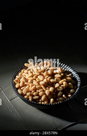 a ceramic bowl full of shelled pine nuts on a gray textured concrete surface fading in the dark and some blank space on top Stock Photo