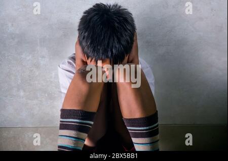 lifestyle dramatic bullying victim portrait of young sad and scared hispanic kid 7 - 10 years old in school uniform sitting alone crying depressed and Stock Photo