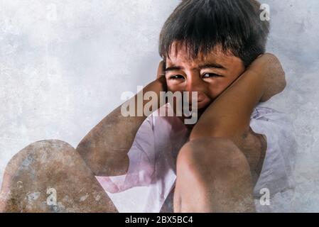 lifestyle dramatic bullying victim portrait of young sad and scared hispanic kid 7 - 10 years old in school uniform sitting alone crying depressed and Stock Photo