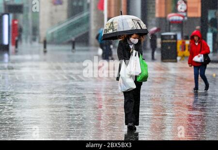 A shopper walks through the rain with an umbrella after a change in the weather has seen the mini heatwave come to an end. Stock Photo