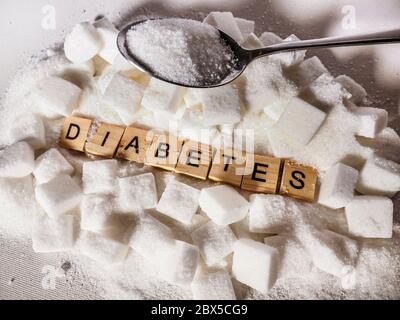 conceptual still life with pile of sugar cubes and diabetes word in block letters as advise on glucose excess and sweet unhealthy food abuse causing a Stock Photo