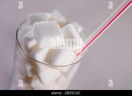 conceptual macro still life image of refreshment glass full of sugar cubes and straw isolated on white background in glucose addiction unhealthy exces Stock Photo
