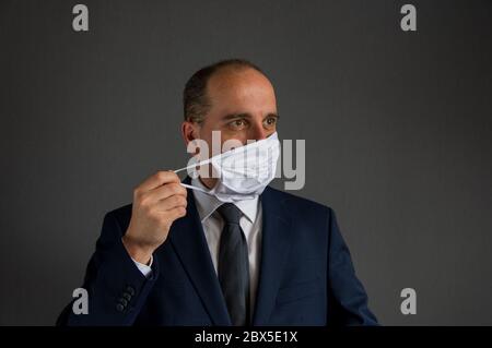 portrait of a smart dressed business man with suit and tie taking off his protective face mask looks into the distance off camera. Concept of hope for Stock Photo