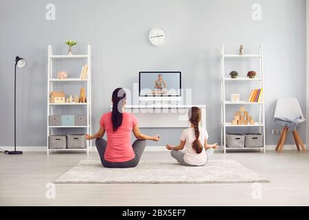 Yoga practice family. Mother and girl practice yoga meditation online training video trainer sitting on the floor in the room. Stock Photo