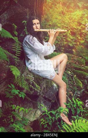 Beautiful dryad playing flute in a forest after the rain. Romance and fantasy Stock Photo