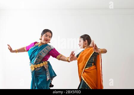 Bharatnatyam dancer performing with her student in front of a plain background. Stock Photo
