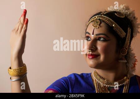 Bharatnatyam dancer looking at her palm while standing in front of a plain background. Stock Photo