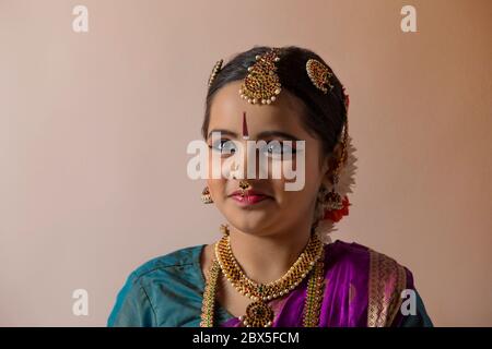 Young bharatnatyam dancer standing in front of a plain background and smiling. Stock Photo
