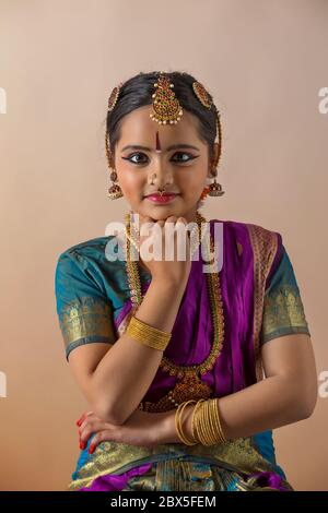 Young bharatnatyam dancer standing gracefully in front of a plain background and smiling. Stock Photo