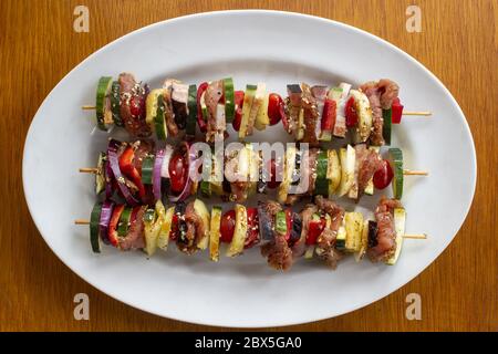 Skewer before grilling composed of bacon onions tomatoes meat pork zucchini peppers on a plate on a wooden table Stock Photo