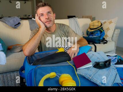 young attractive and happy man at home couch preparing travel back and packing suitcase folding clothes and organizing passport and things excited bef Stock Photo