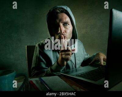 dangerous looking young hacker man in hoodie typing on laptop computer hacking and decoding system data or having illegal access breaking password on Stock Photo