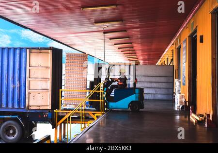 Container unstuffing, forklift carries pallets of cargo from container to put in warehouse. Forklift, driver, pallets of cargo, and container on truck. Stock Photo