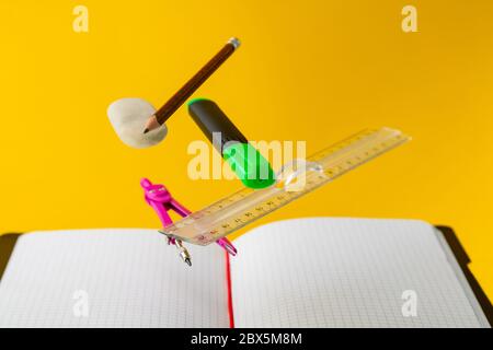Levitating school supplies for math - notebook, pen, ruler, pencil, divider and eraser on yellow background. Concept of education and creativity Stock Photo