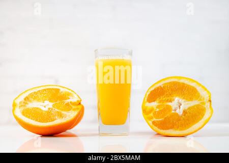 Freshly squeezed orange juice in a glass on a table with slices of oranges next to it. Refreshing yellow beverage with fruits on white background Stock Photo