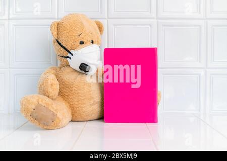 Teddy bear with face mask and pink note book on white background. Concept of home school, isolation. Staying at home. Corona virus. Stock Photo