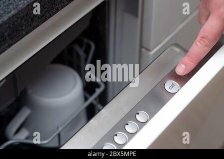 Close up of finger pressing start button on dishwasher in the kitchen. Hand starting dish washer machine Stock Photo