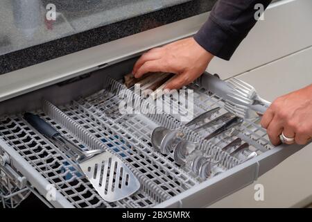 Close up of hand unloading dish washer in the kitchen. Person taking of appliances of full shelf of dishwasher. Stock Photo