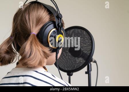 Closeup of teenager recording music in home studio. Girl with headphones and microphone recording song Stock Photo