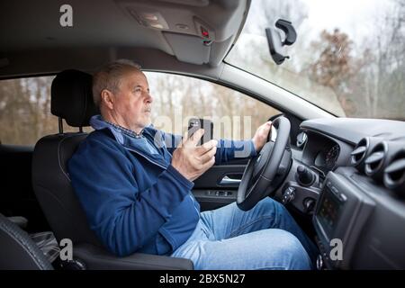 Senior man using a smartphone while riding his new, modern car, transportation concept Stock Photo