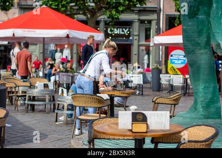 Zwolle, Netherlands. Waitress cleans a table on restaurant terrace with disinfectant alcohol spray. The terraces were allowed to open again Stock Photo