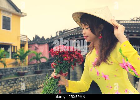 Selective focus on red flowers, beautiful women in Ao Dai Vietnam traditional dress holidng a branch of red flowers Stock Photo