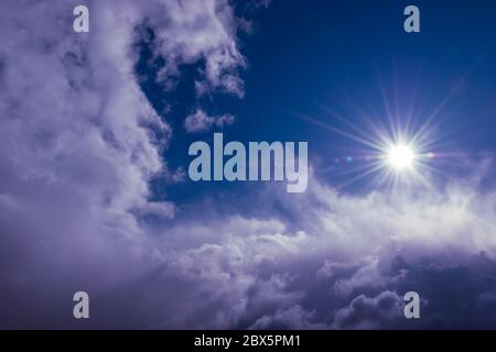 natural sun shines over clouds in deep blue stormy sky Stock Photo