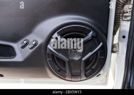 Close-up of an open front door of a Russian car with a new factory-made music speaker on a black plastic panel and with power window buttons nearby. Stock Photo