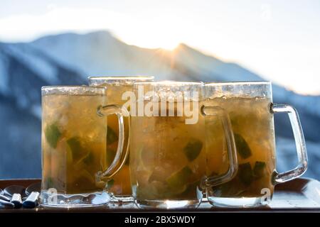 Four huge glasses with caipirinha drink against snow covered mountains and sunlight Stock Photo