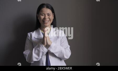 Happy doctor laughs joyfully clasped her hands together while standing against the gray wall. Beautiful brunette in medical uniform rejoices at the Stock Photo