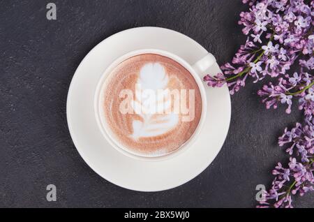 Lilac, coffee with latte art and marshmallows on black table. Romantic Flat lay with copy space Stock Photo