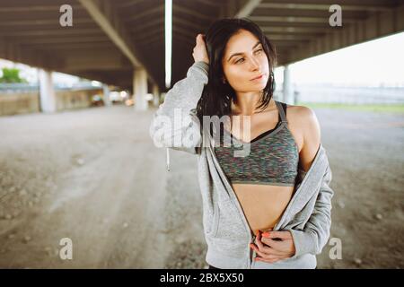 Beautiful young fit woman in sportswear posing with urban view under a bridge. Beauty and sport concept. Stock Photo