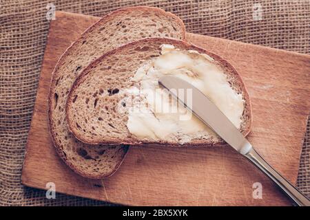 Close-up slice of bread with butter and knife on the wooden desk, poverty concept Stock Photo