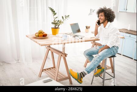 Creative man talks on mobile phone working from home. Young Arab guy in casual works in studio home kitchen interior. Toned image Stock Photo