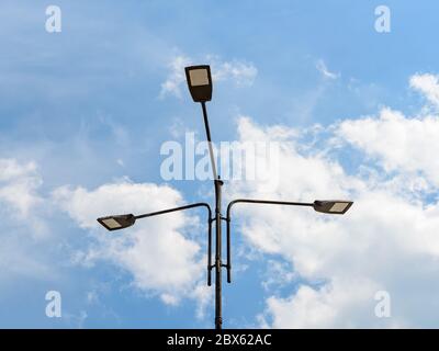 Three led street lights on a pole against blue sky with light clouds. Modern energy-saving technology for lighting streets and roads. Led street lamp. Stock Photo