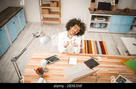 Jolly young businessman took break from work. Cheerful arab guy play with pencils looking at camera while sitting at workplace in studio room. High Stock Photo
