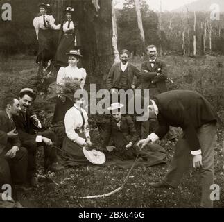 A group out bushwalking posing for the camera in Victoria, Australia c. 1900. Having come across a dead snake, one man gingerly picks it up by its tail. The women and men are fashionably dressed in quite formal attire for such an outing. They are surrounded by gum trees (Eucalyptus) and ferns. Stock Photo