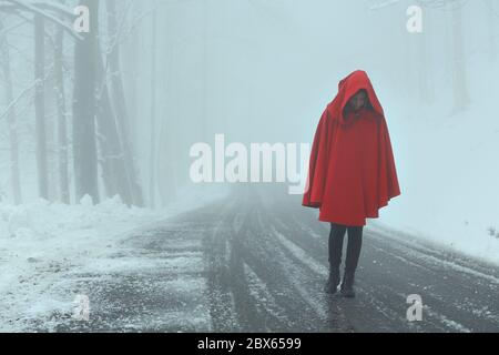 Woman walking alone on snowy and misty road Stock Photo