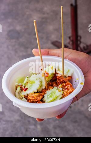 Tod Mun Kala in foam cup, Thai cuisine served with cucumber and sweet sour sauce with crispy crunchy fried holy basil leaves. Stock Photo