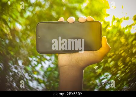 Boy hand showing mobile smart phone screen Isolated on Blur green nature background. Stock Photo
