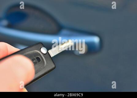 Closeup of hand holding a remote key unlocking the blue car. Stock Photo