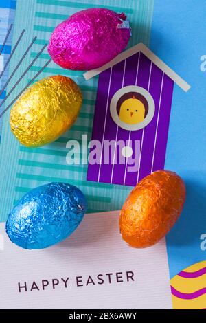 solid milk chocolate mini Easter eggs foil wrapped with chick looking out of bird box background - looking down on from above Stock Photo